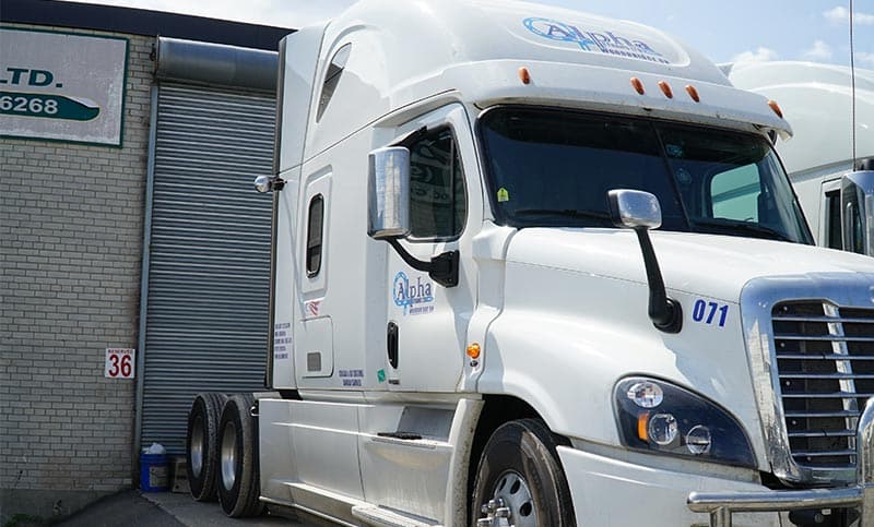 Alpha Trans unit 071, a white Freightliner Cascadia in company livery, parked at a shop bay door